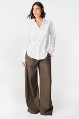 Camisa blanca de algodón con cuello clásico y cierre frontal de botones. Presenta un diseño con tablas verticales en el frente, corte redondeado en los laterales y puños anchos desmontables.