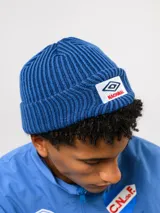 Gorro tipo beanie de punto acanalado en color azul, con parche frontal bordado que incluye el logo de Umbro y la palabra Nacional.