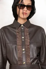 Campera de cuero color marrón con cuello clásico, cierre frontal con botones metálicos y detalles de volados en gamuza a lo largo de la botonadura y en los puños.