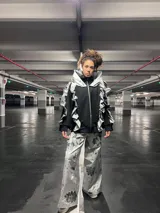 Conjunto de saco y pantalón plateado con estampado de flores negras. El saco es de corte deportivo con cierre y volados en el cuello y mangas. El pantalón es de corte ancho.