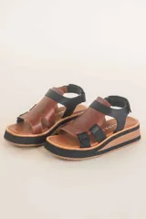 Sandalias de cuero color marrón con plataforma de madera y suela de goma negra. Tiras anchas de cuero marrón en el empeine y tobillo con ajuste de hebilla.