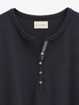 Remera de algodón con spandex, color negro, de manga larga y ajuste al cuerpo. Presenta un escote redondo con cartera frontal de botones y detalle de cordón decorativo en contratono.