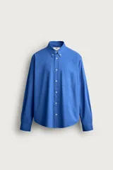 Camisa de corte relajado confeccionada en tejido de algodón de color azul, con cuello abotonado, manga larga, bolsillo frontal de parche y cierre de botones.