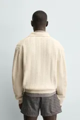 Cárdigan de ajuste relajado, tejido en hilado con lana, color crema. Presenta cuello solapa, manga larga y textura de punto trenzado en todo el cuerpo. Cierre frontal con botones.