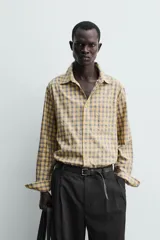 Camisa relaxed fit de algodón con elasticidad, color amarillo y gris a cuadros. Tiene cuello solapa, manga larga con puño abotonado, bajo con aberturas laterales y cierre frontal de botonadura.