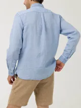 Camisa celeste de lino con cuello camisero, manga larga, cierre con botones y bolsillo en el pecho.