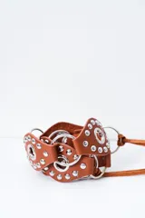 Cinto de cuero color camel con tachas metálicas plateadas y argollas, complementado con tiras finas para anudar.