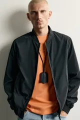 Cazadora bomber de tejido técnico ligero color marrón oscuro, con corte regular fit, cuello, puños y ruedo de rib elástico, bolsillos frontales de vivo y cierre frontal con cremallera.