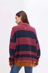 Buzo de punto con diseño de rayas horizontales en tonos bordó, azul marino y mostaza. Presenta cuello tipo polo con cartera de botones, mangas largas y calce holgado.