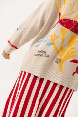 Saco oversize tejido con ilustraciones inspiradas en corales, peces, estrellas de mar y tortugas. Presenta galón picot en rojo en cartera y puños, y botones a tono.