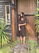 Vestido midi de lino color azul, con escote en V, mangas cortas y falda amplia de corte escalonado. Presenta detalles de costuras y bordes en tono rojizo contrastante.