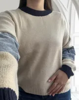 Sweater beige de tejido de punto con cuello redondo y puños en color azul marino. Mangas largas con parches de denim en los antebrazos.