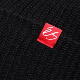 Gorro de lana éS modelo Block Beanie, color negro, con diseño tejido de canalé y pequeña etiqueta roja con el logo de la marca en el doblez.
