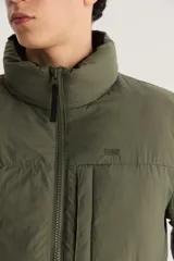 Campera puffer verde militar con cuello alto, cierre frontal con cremallera y bolsillo pequeño en el pecho.