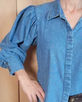 Camisa de jean azul con mangas largas abullonadas, puños ajustados y cuello clásico.