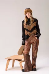 Sweater de punto color crema con cuello medio alto y silueta relajada. Presenta un diseño frontal con líneas en V decoradas con flecos largos de color marrón aplicados a mano.