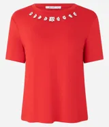 Blusa blanca de mangas cortas confeccionada en viscosa con cuello redondo con brillos en formas florales.