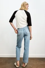 Jeans de mujer, tiro alto, color azul medio con efecto desgastado (lavado claro en muslos y oscuro en bordes). Corte recto y ancho (mom fit) con cinco bolsillos y cierre frontal de botón y cremallera.