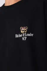 Remera de corte oversize color gris oscuro, confeccionada en algodón premium de alto gramaje. Presenta un diseño minimalista con un pequeño estampado frontal que incluye un oso y el texto 'Richer & Louder VCP'.
