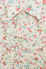 Camisa entallada de manga larga con estampado floral en tonos rosados y azules sobre fondo crema. Presenta cuello solapa, puños abotonados y volantes decorativos en el frente, con cierre de botones.