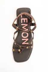 Sandalias planas de cuero marrón, con tiras finas decoradas con tachas metálicas redondas y tira ajustable alrededor del tobillo.