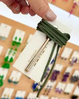 Gargantilla tipo choker con cordón de gamuza verde oscuro, dije tubular plateado y cuentas plateadas en los extremos.