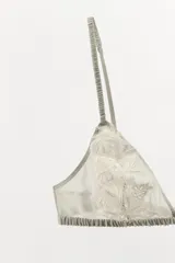 Sujetador triangular de escote en pico con tirantes finos ajustables y cierre posterior con gancho metálico. Presenta un diseño de encaje floral a tono sobre una base de tul semitransparente.