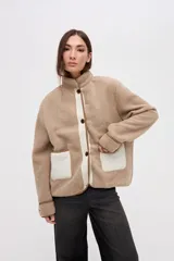 Campera de sherpa doble faz en color crema con detalles en verde oliva. Presenta cierre frontal con botones, bolsillos laterales de nylon capitoneado y terminaciones en contratono. Diseño de calce relajado con bordado en la manga.