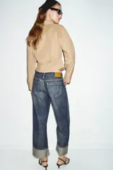 Jeans de tiro medio con corte relax fit y pernera holgada. Presenta diseño de cinco bolsillos, cierre frontal con cremallera y botón, y bajo con vuelta marcada.