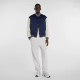 Campera estilo varsity con cuerpo azul marino y mangas en color beige. Presenta cierre frontal con botones a presión, cuello, puños y ruedo acanalados con rayas decorativas, y logo de la marca bordado en el pecho.