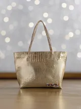 Bolso shopper de cuero color dorado con textura crocco, asas de hombro en tono semi natural y cierre superior. Cuenta con diseño espacioso, bolsillo interior y detalle artístico exclusivo de la marca.
