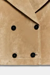 Trench corto de Zara confeccionado en piel de ante, con cuello de solapa, cierre frontal cruzado con botones, mangas largas con trabillas y bolsillos delanteros de vivo.