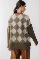 Saco tipo cardigan de punto con diseño de rombos en tonos marrón chocolate y beige. Presenta cierre frontal con botones grandes, cuello en V con borde en color rojo, dos bolsillos delanteros con ribete rojo y detalles bordados pequeños. Posee mangas largas con una franja horizontal en color mostaza cerca del puño.