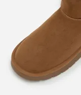 Bota de caña media color marrón, confeccionada en poliéster con acabado suave. Cuenta con interior forrado en piel sintética para mayor abrigo, tirador trasero y suela plana de goma con diseño dentado.