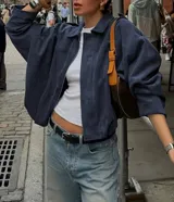 Chaqueta tipo bomber de calce holgado y silueta relajada, confeccionada en gamuza color azul marino. Presenta cuello camisero, cierre frontal oculto y mangas amplias con puños rectos.