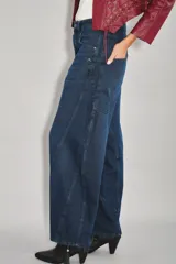 Jean de tiro medio-alto con calce holgado y relajado. Presenta piernas amplias con recortes curvos que se estrechan hacia el tobillo, creando una silueta tipo barril. Confeccionado en denim rígido color azul con sobreteñido negro, cuenta con cierre, botón y bolsillos traseros desplazados hacia el frente.