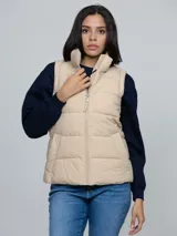 Chaleco acolchado de cuello alto con cierre frontal de cremallera y dos bolsillos laterales de ojal. Presenta un diseño moderno y ligero, con detalles distintivos de la marca.