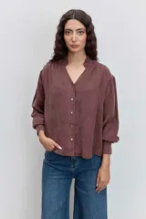 Camisa de satén color azul grisáceo, con cuello mao con detalle de volados, cierre frontal con botones y mangas largas con puños abotonados.