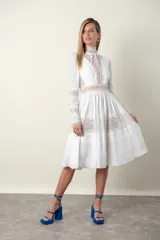 Vestido midi blanco con detalles de encaje color beige en cuello, mangas, cintura y ruedo. Tiene cuello alto con lazo y mangas largas.