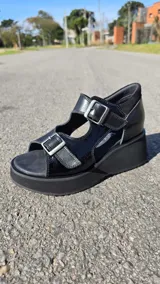 Sandalias de cuero color tostado con plataforma y taco chino, tiras frontales y laterales con hebillas ajustables y detalles en tono dorado texturizado.
