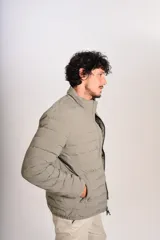 Campera puffer de corte clásico en color beige, con cierre frontal, cuello alto y puños elásticos. Presenta un diseño acolchado horizontal y un pequeño logo bordado en el pecho.