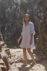 Vestido camisero corto color gris, con cuello clásico, cierre frontal de botones y mangas tres cuartos con volados en los puños.