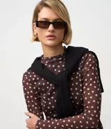 Blusa de manga larga ajustada al cuerpo, confeccionada en tul marrón con estampado de lunares blancos. Presenta cuello redondo y un cárdigan negro cruzado sobre los hombros.