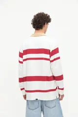 Remera polo de manga larga con diseño de rayas horizontales rojas sobre fondo blanco, cuello camisero tostado con media cartera de botones y puños ajustados.