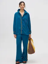 Camisa azul de corte holgado, con cuello camisero, mangas largas con detalles en los puños, bolsillo frontal con bordado y cierre delantero con botones.