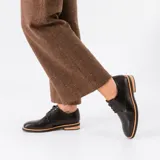Zapato mocasín de cuero vacuno color negro, con cordones y punta redonda. Tiene taco de madera foliado en cuero de 2,5 cm y entre suela de goma de 1 cm.