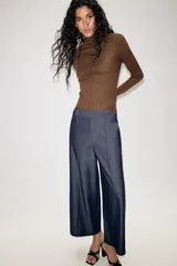 Pantalón culotte de tiro medio con pernera ancha y corta. Presenta nervios marcados en la parte delantera, bolsillos laterales y cierre frontal con cremallera, botón interior y hebilla ajustable en la cintura.