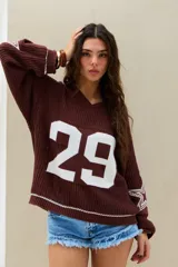 Sweater de punto marrón chocolate, con diseño oversize, cuello en V, mangas largas con estrellas blancas estampadas y número grande en el frente.