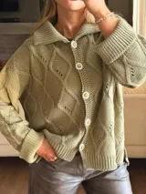 Saco tejido en color verde oliva con diseño de ochos y trenzas. Presenta cuello estilo camisero, cierre frontal con botones tipo joya, mangas holgadas y silueta oversize.