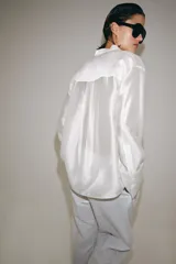Camisa de cuello redondo y manga larga con puños anchos. Presenta un bolsillo de plastrón en el pecho con detalles de bordados a tono, los cuales también se encuentran en los puños. Cierre frontal con botones ocultos por tapeta.